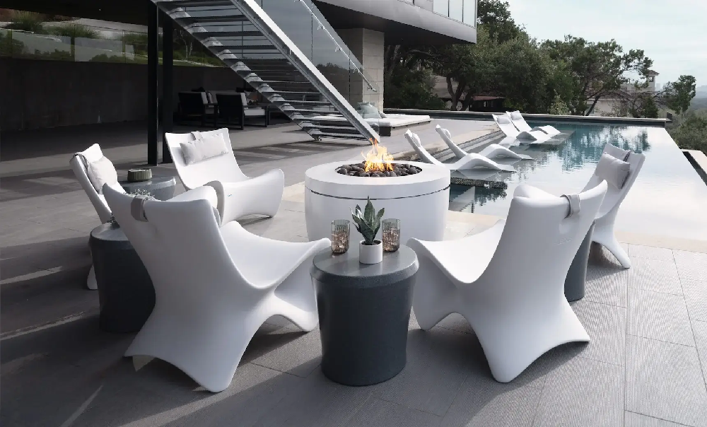 Designer outdoor lounge chairs and fire pit beside an infinity pool creating an upscale resort-inspired pool deck gathering space.